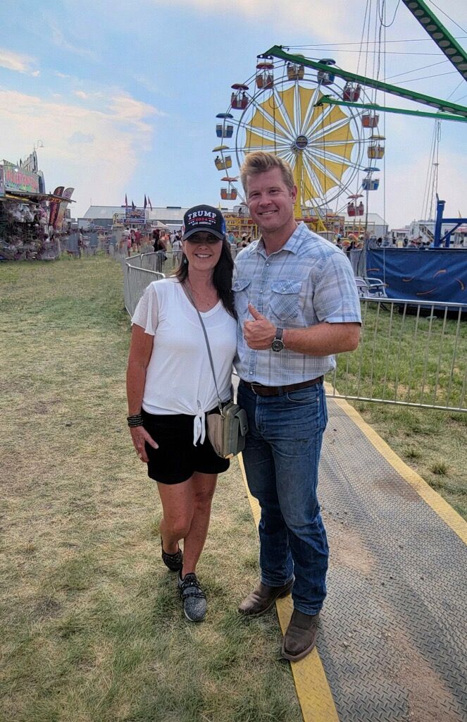 A man and a woman are standing in front of a ferris wheel at a carnival.