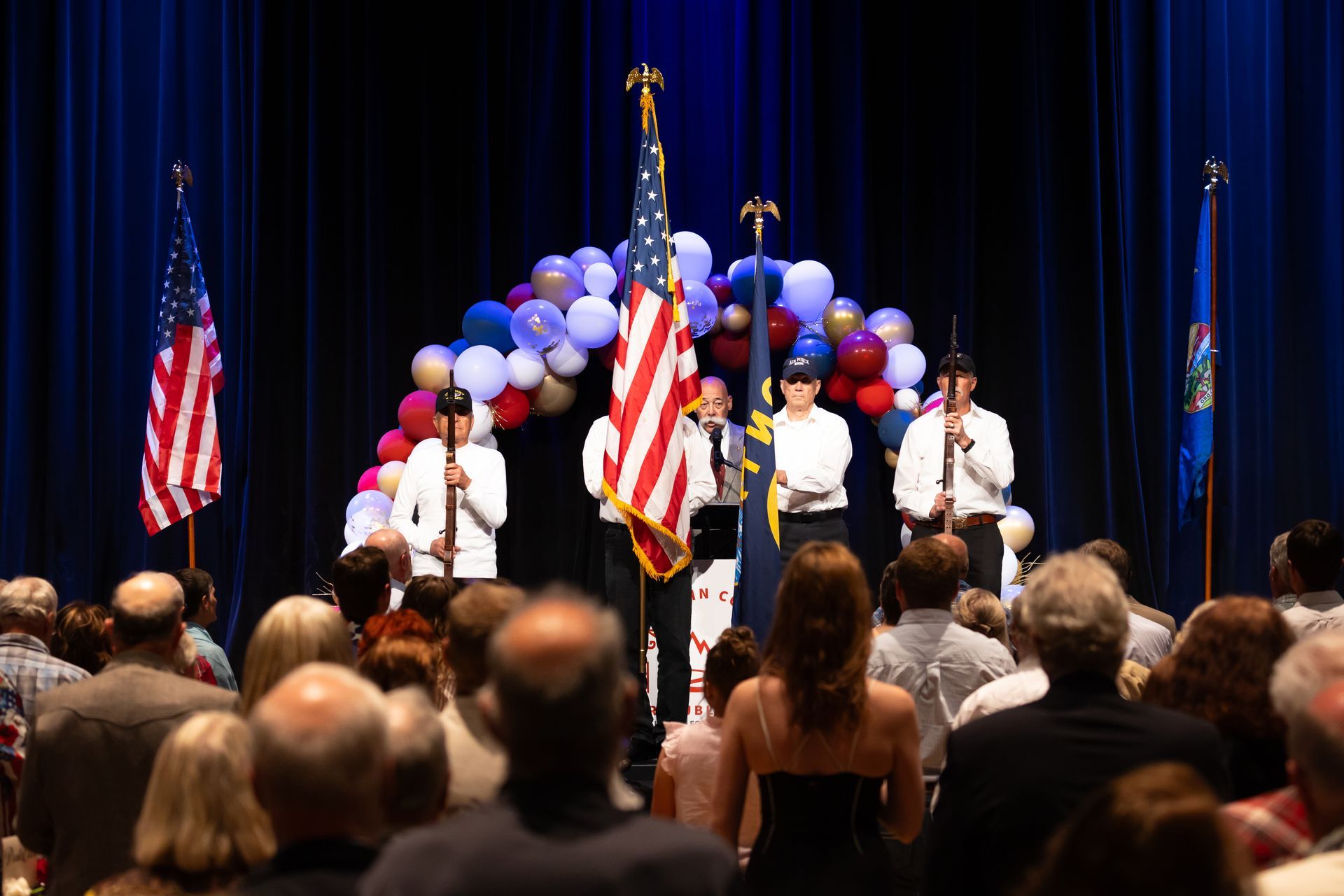 A group of people are standing on a stage with flags and balloons.