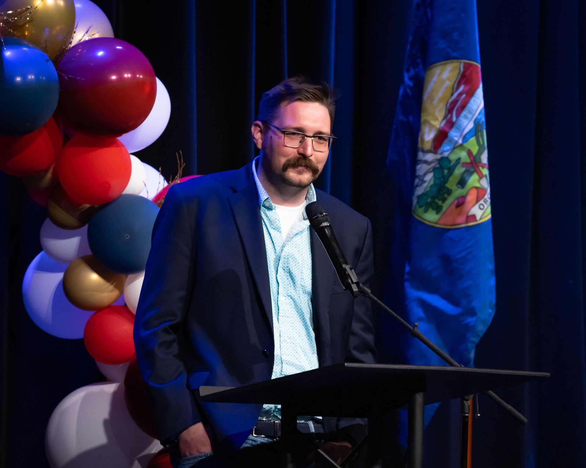 A man in a suit is standing at a podium speaking into a microphone.