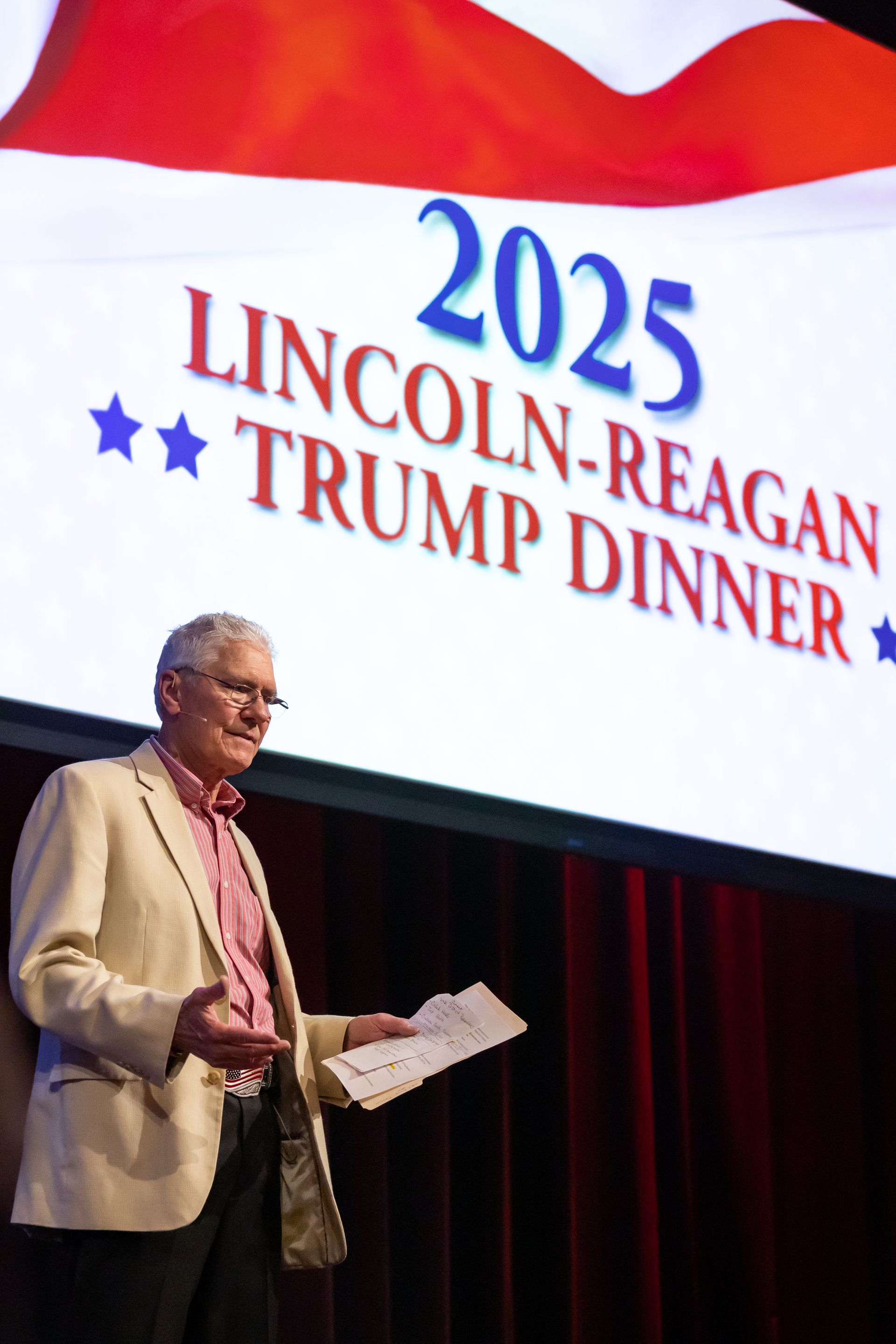 A man in a white suite in front of a sign for the Lincoln-Reagan-Trump Dinner