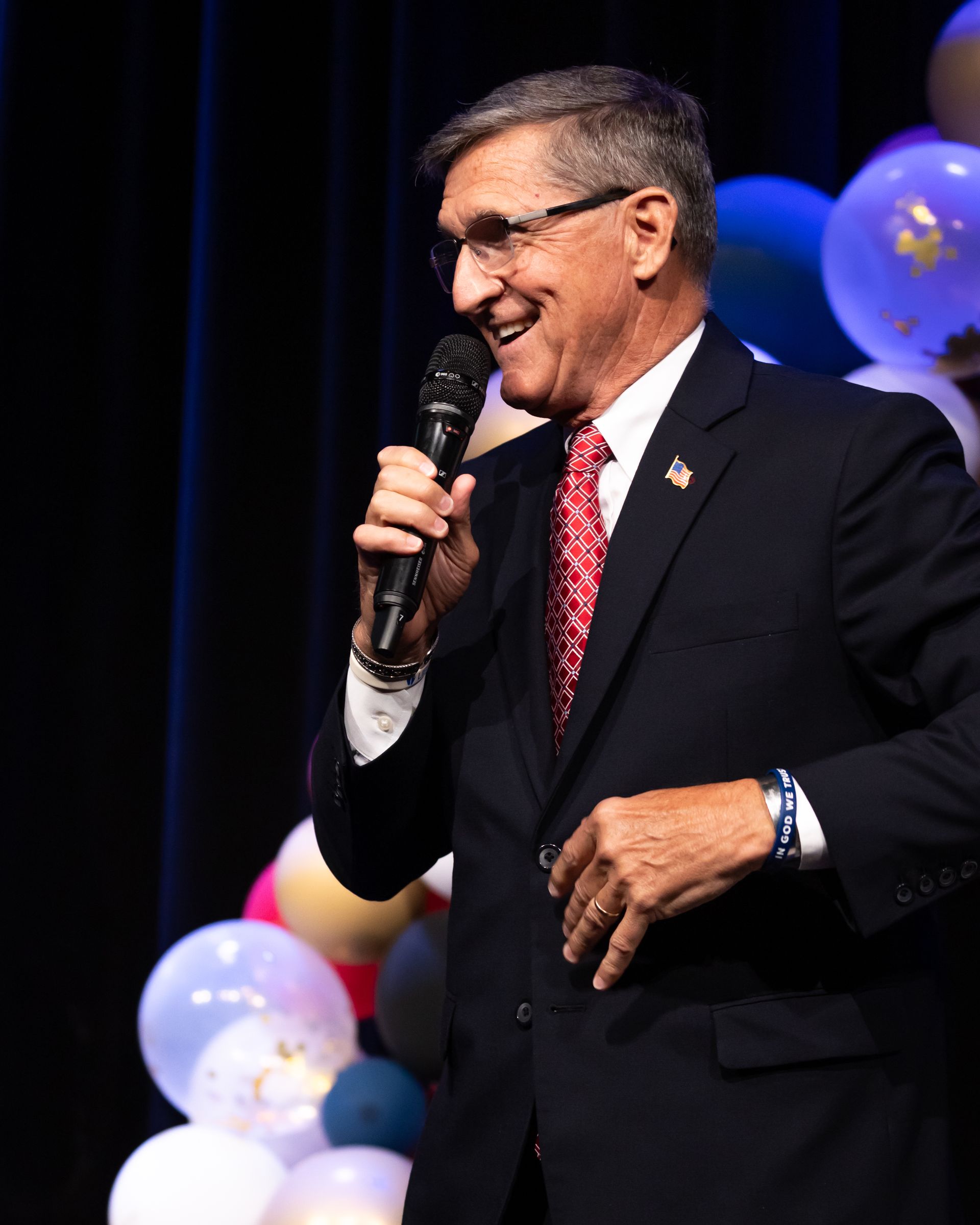 A man in a suit and tie is holding a microphone in front of balloons.