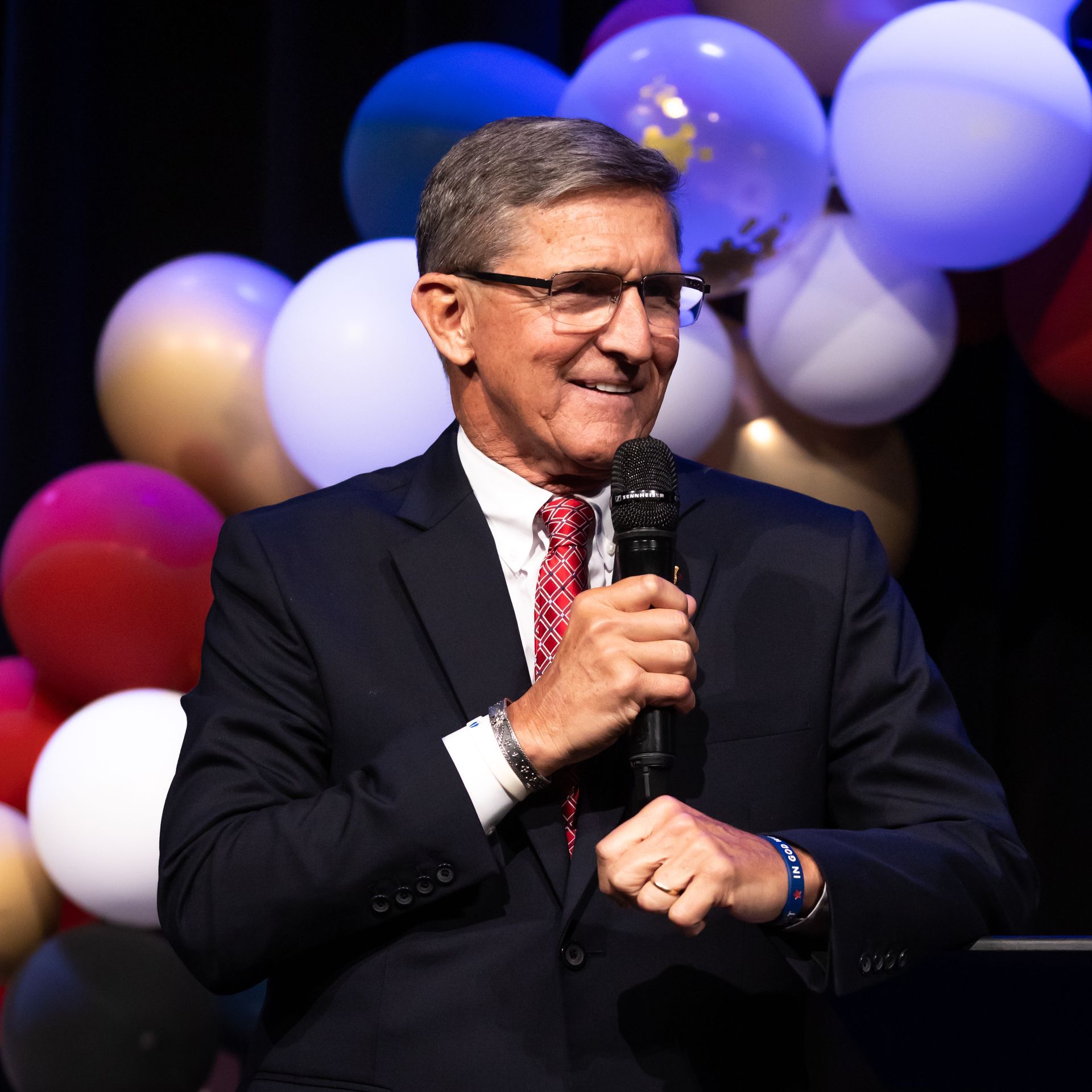 A man in a suit and tie is holding a microphone in front of balloons