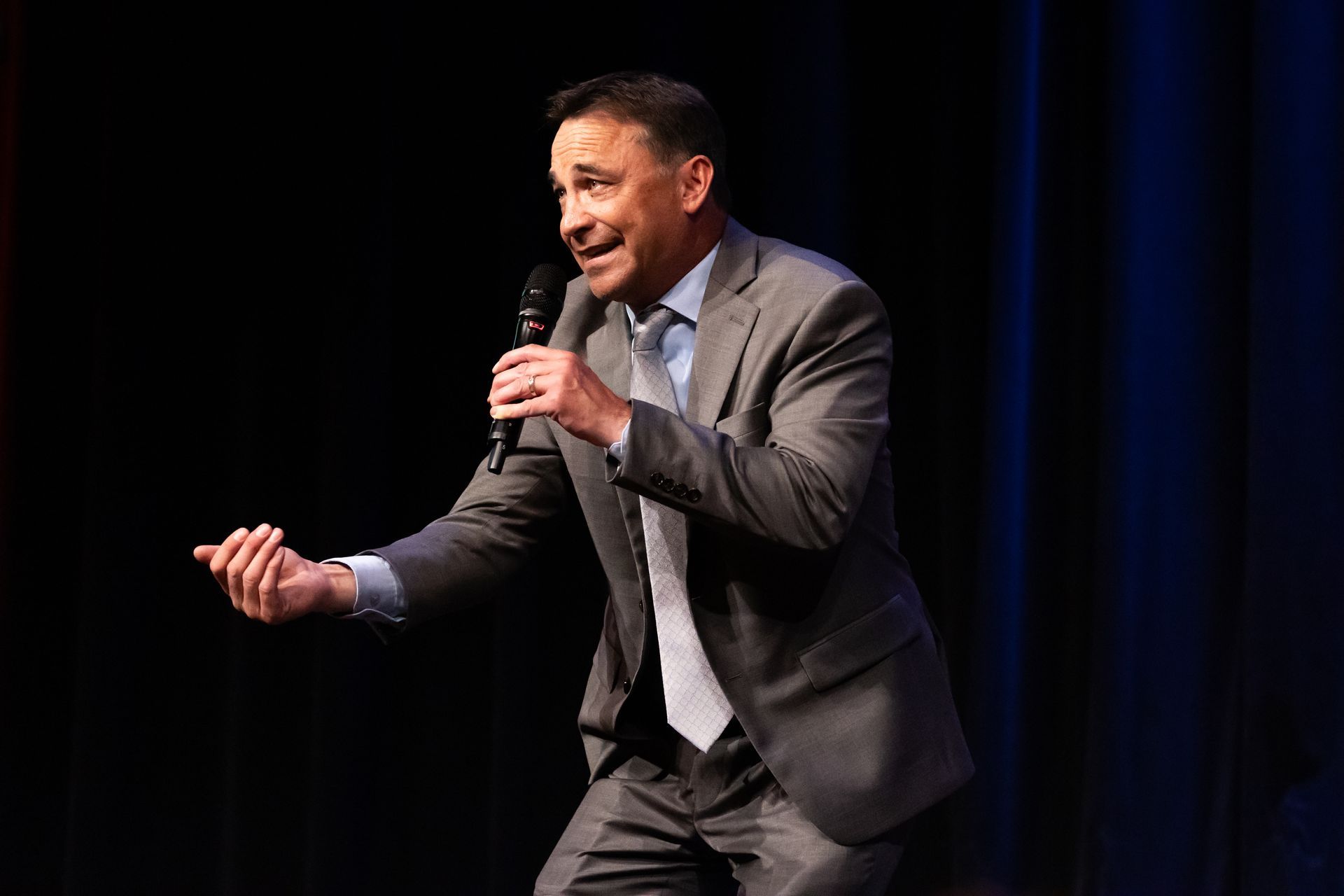 A man in a suit is holding a microphone on a stage.
