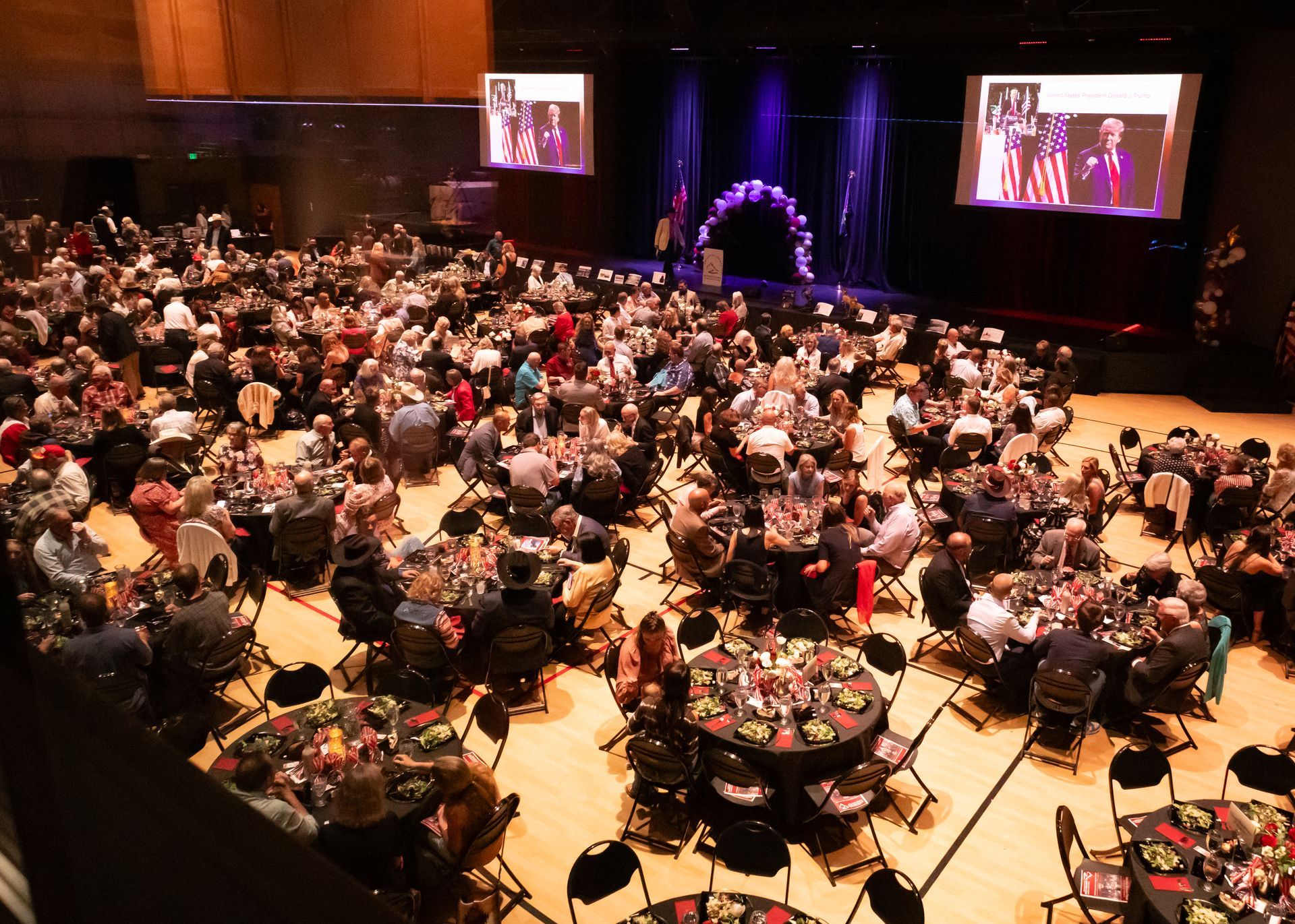 A large crowd of people are sitting at tables in a large auditorium.