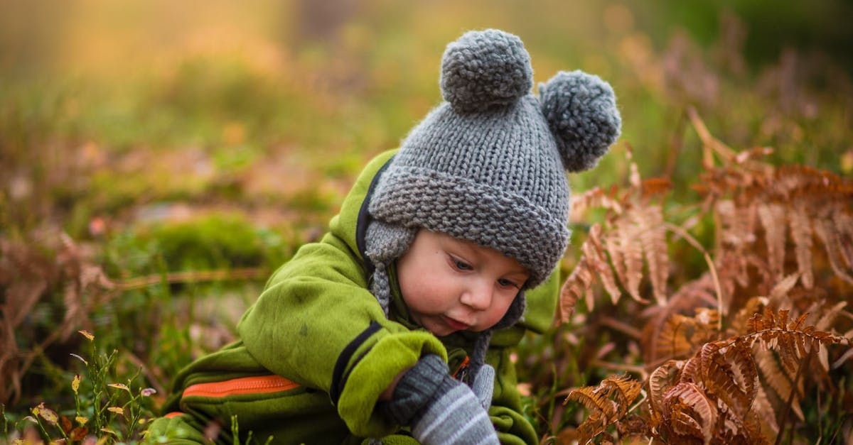 A little boy wearing a knitted hat and gloves is playing in the grass.