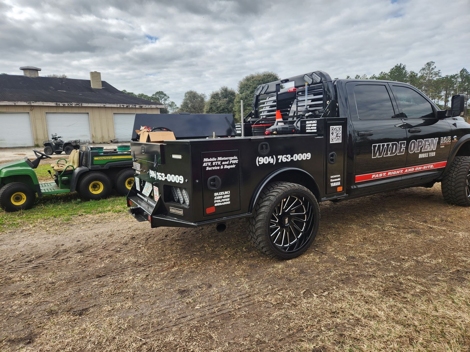 Black work truck with toolboxes parked on dirt. A green John Deere tractor is in the background.