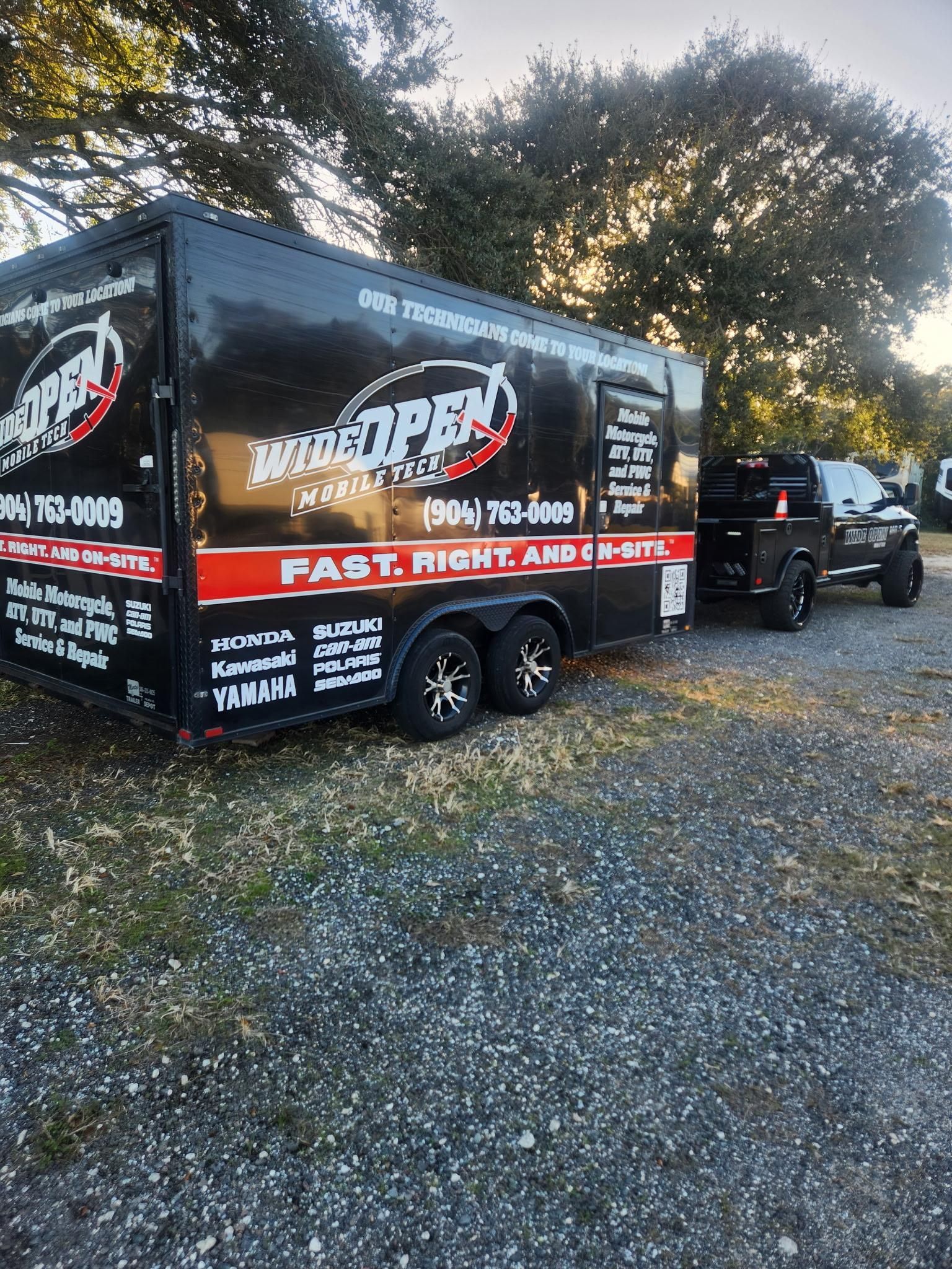 Black trailer with red and white logo and truck parked on gravel.