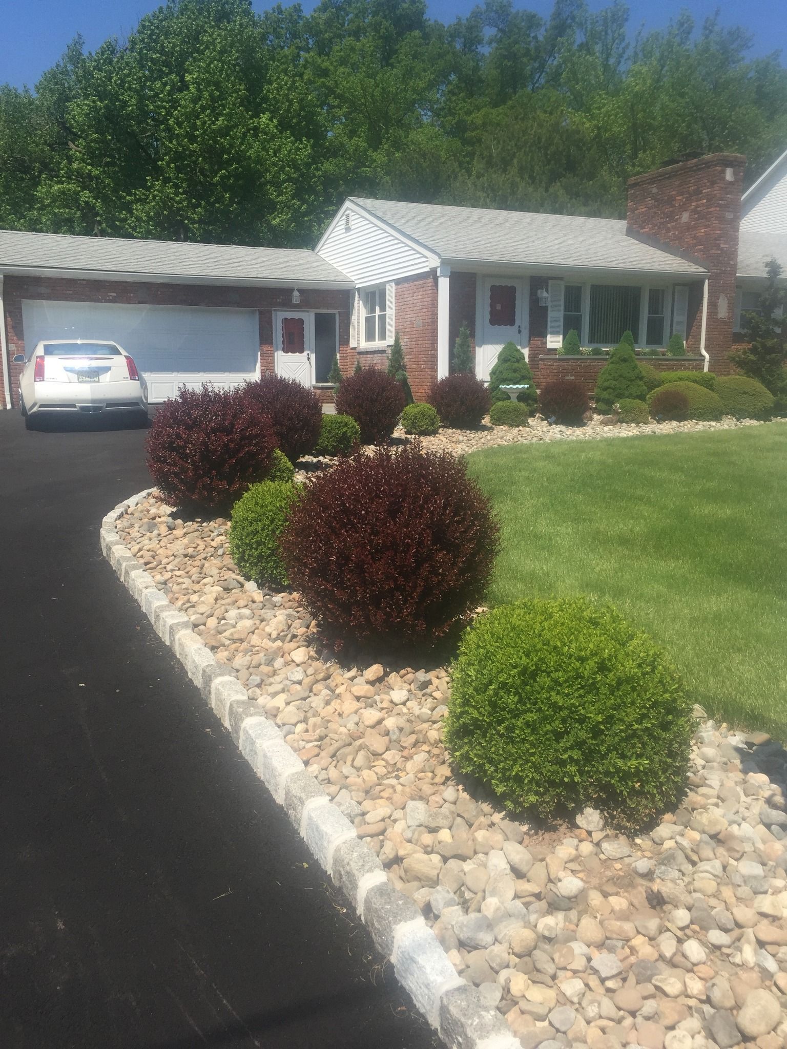A house with a driveway and landscaped yard, featuring shrubs and a car.