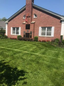 Brick building with a red cross, flanked by windows with white shutters and a green lawn.