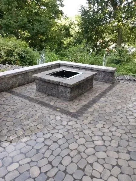 Stone patio with a square fire pit and low retaining walls, surrounded by trees.