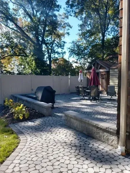 Backyard patio with stone path, grill, seating, shed, and trees.
