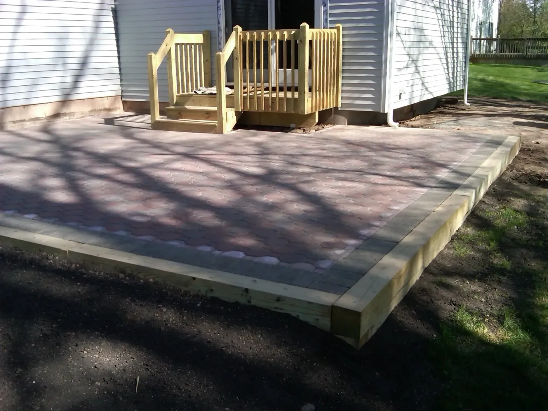 Brick patio with wooden border and small wooden deck with stairs leading to a house.