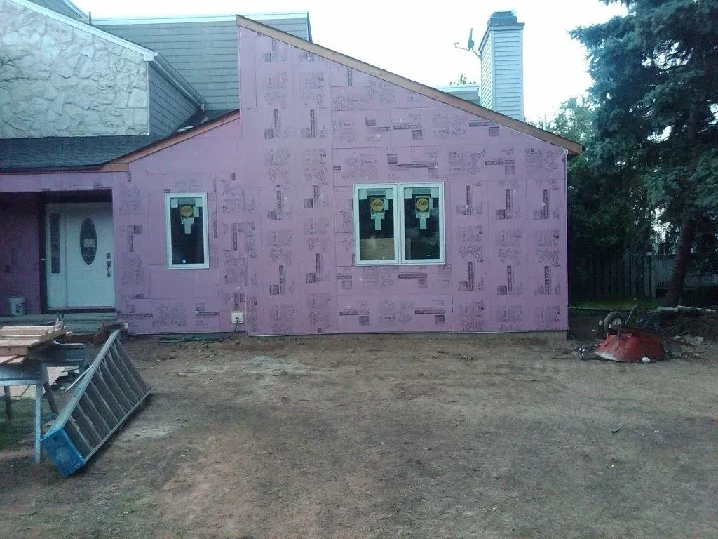 House exterior under construction, pink insulation visible, new windows installed.