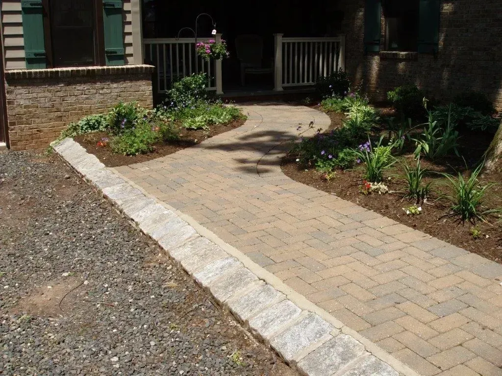 Brick pathway leading to a porch, bordered by gravel and flowerbeds.