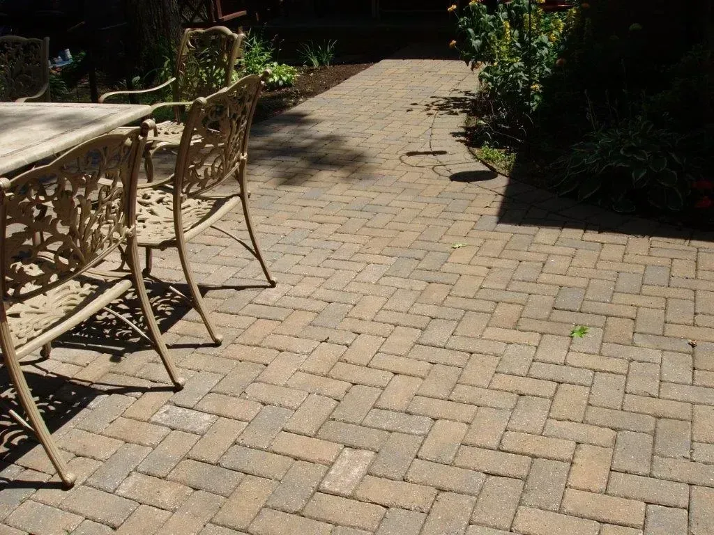 Brick patio with ornate table and chairs; path leads to plants and sunlight.