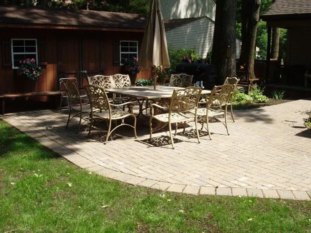 Outdoor patio with table, chairs, and umbrella on brick pavers, next to shed.