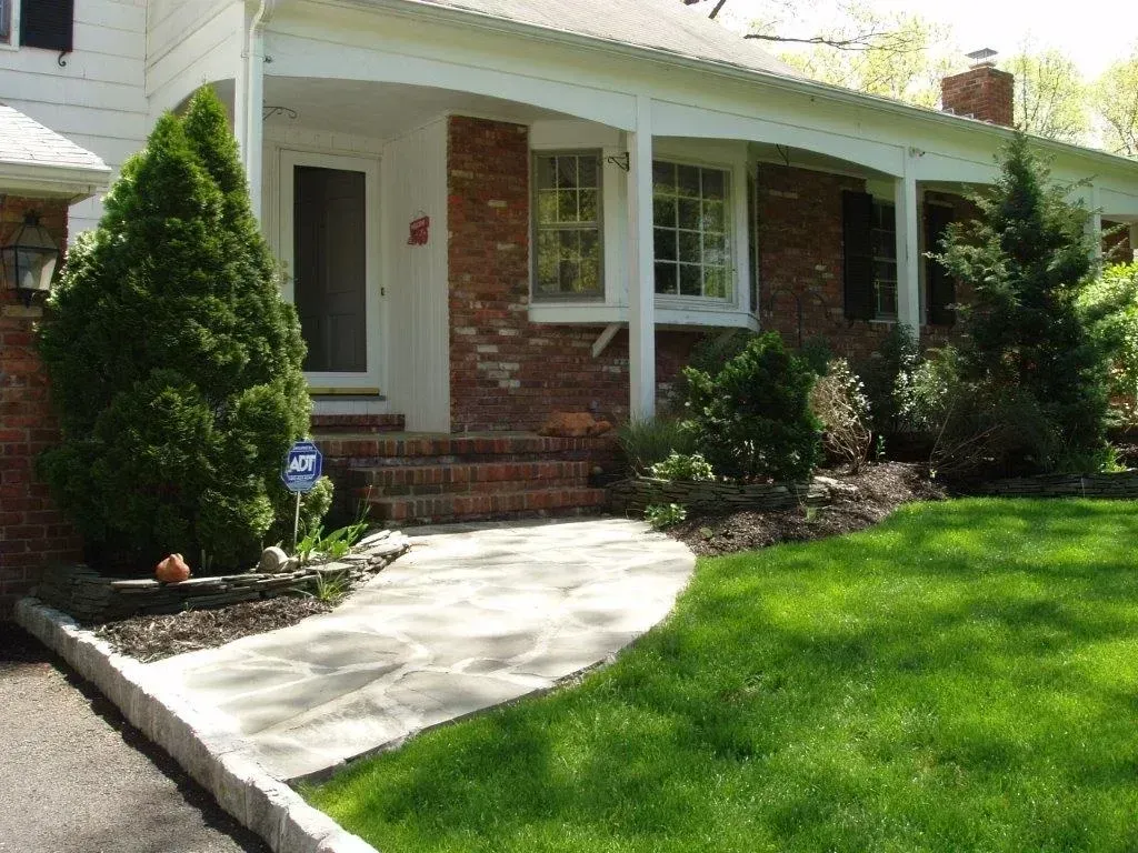 Brick house with covered porch, stone path, green lawn, and shrubs.