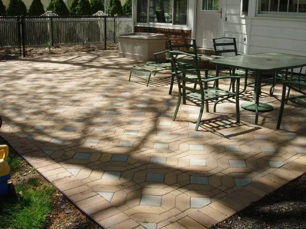 Patio with stone pavers and green metal furniture. Backyard scene, sunny with tree shadows.