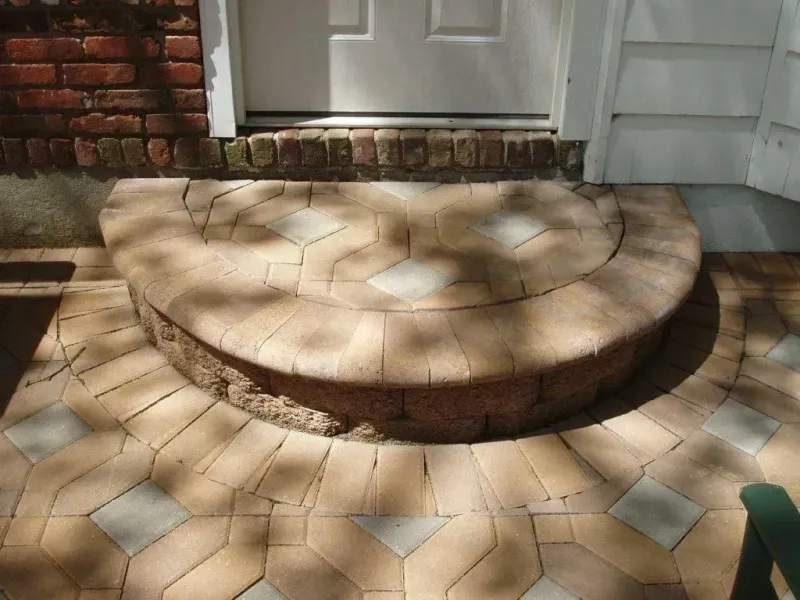 A semi-circular brick step in front of a white door on a patio with patterned paving stones.