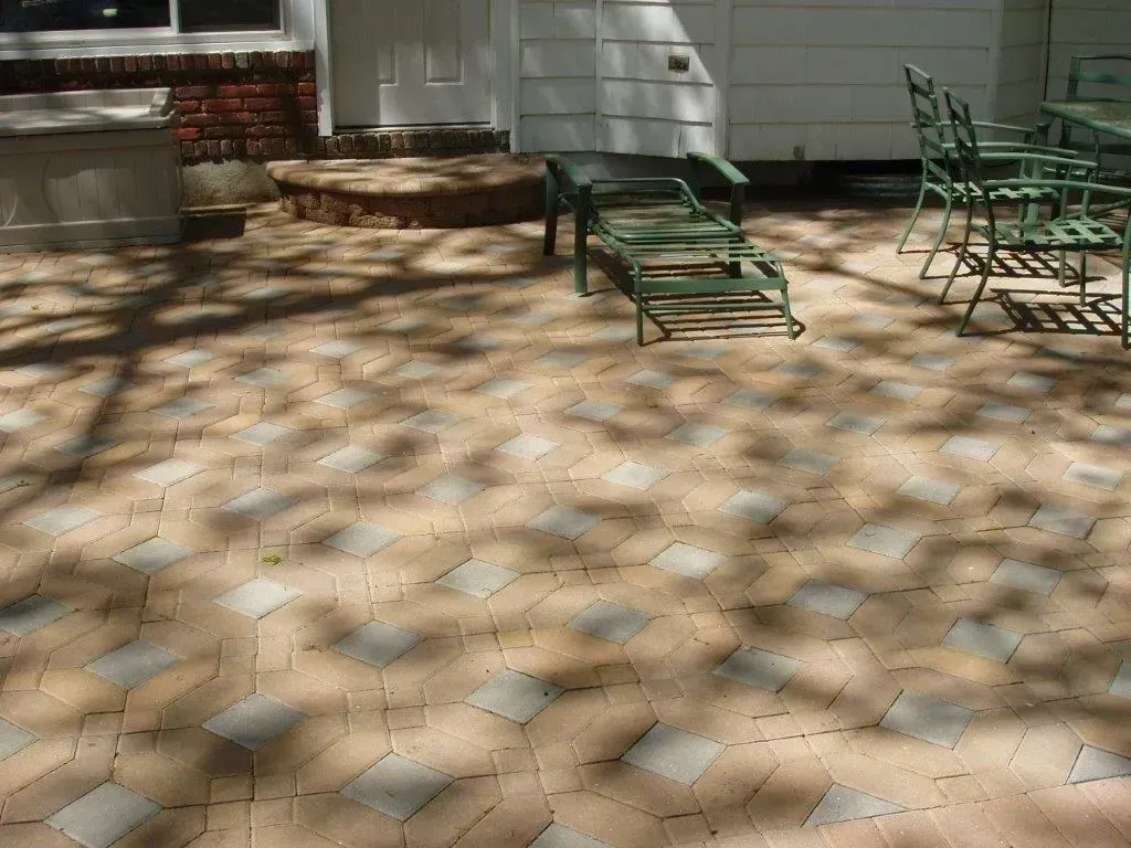 Brick patio with lounge chair and green patio furniture; dappled sunlight.