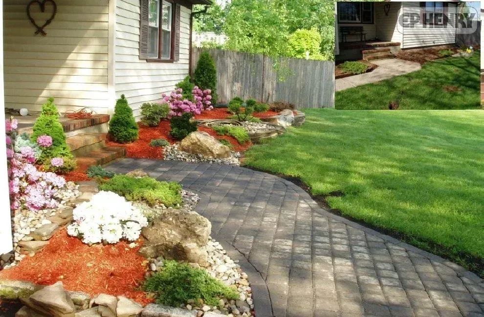 Brick walkway curving through a garden bed with flowers and mulch, next to a lawn. House in the background.