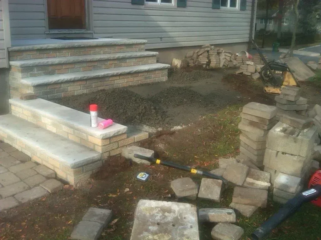 Construction site with concrete steps, brick detailing, and building materials scattered on the ground.
