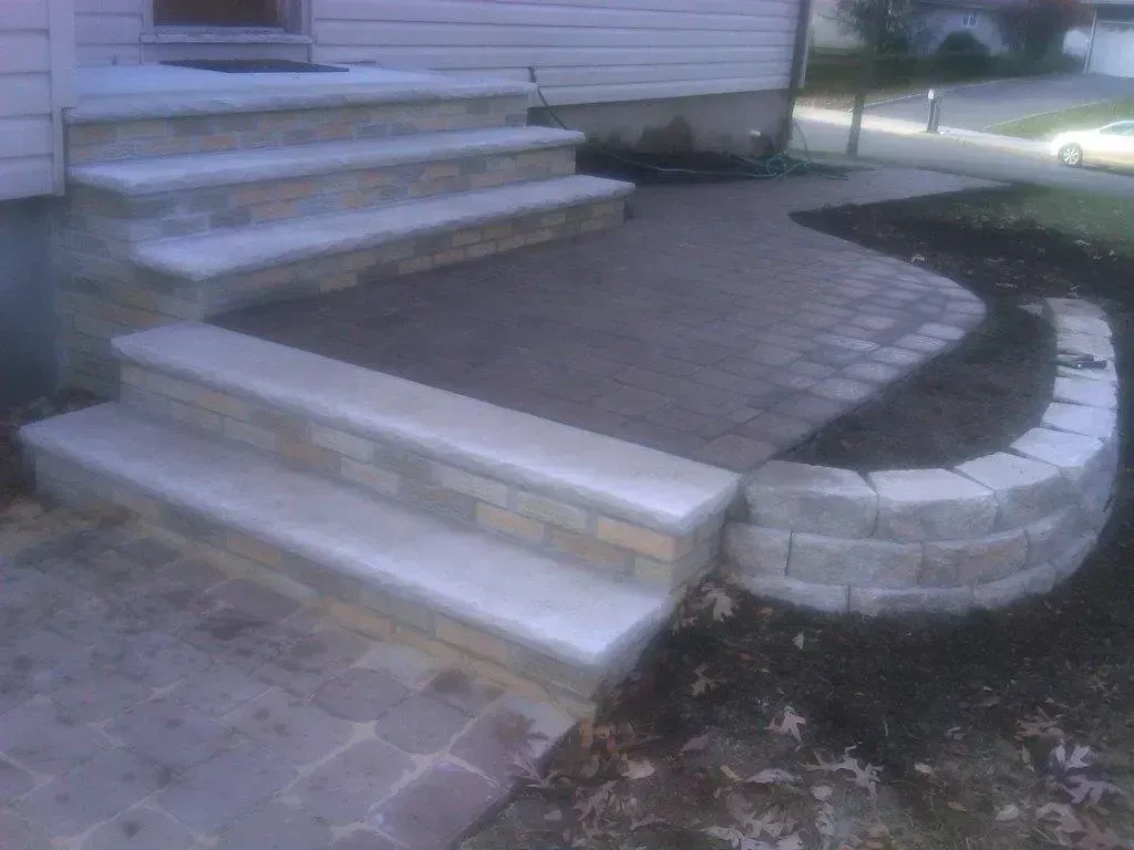 Stone steps and paved patio leading to a house.  Curved stone retaining wall frames a garden bed.