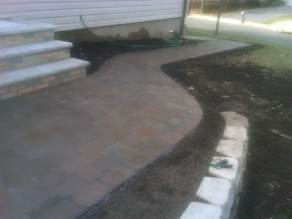 Brick walkway leading from steps to a lawn, with a small retaining wall on the side.