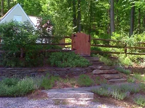 Stone steps lead up to a wooden gate and a small white building, surrounded by greenery.