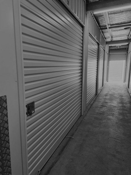 A Black and White Photo of a Hallway With a Row of Garage Doors — Tableland Self Storage In Atherton, QLD