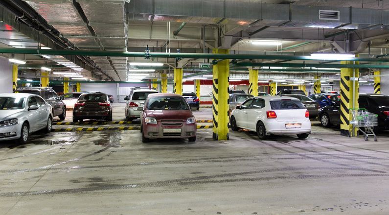 A parking garage filled with cars and a shopping cart.