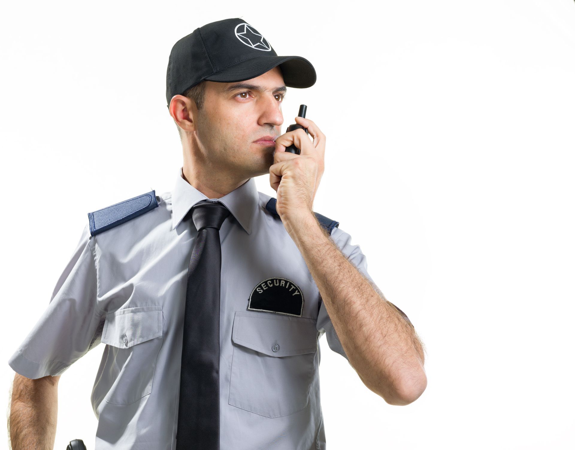 A Caucasian security guard in uniform with cap and tie uses a walkie-talkie