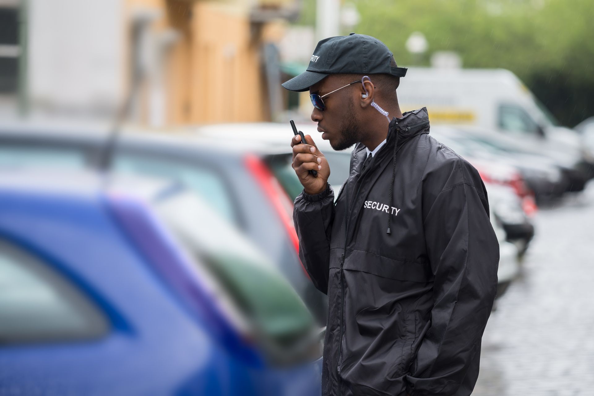 A security guard in a black uniform is using a walkie-talkie on the street.