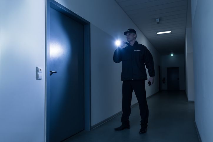 Full length of mature security guard with flashlight standing in front of door in building.