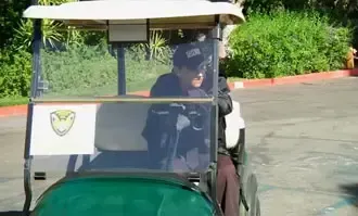 A man is driving a golf cart in a parking lot.