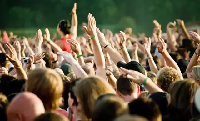 A crowd of people are raising their hands in the air at a concert.