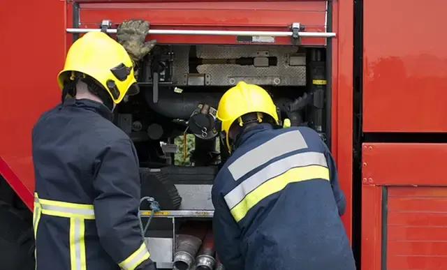 Two firefighters are working on a red fire truck.