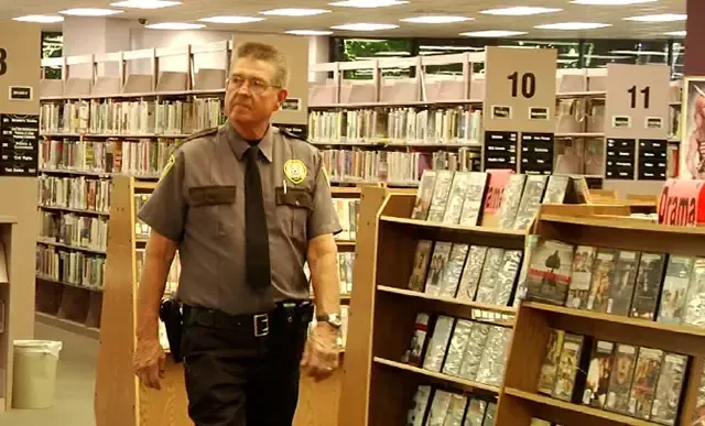 A man in a uniform and tie is standing in a library.