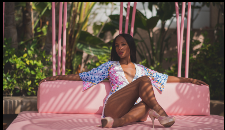A woman is sitting on a pink couch with her legs crossed.