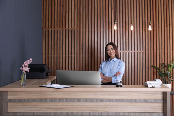 a woman is standing at a reception desk in front of a laptop computer .