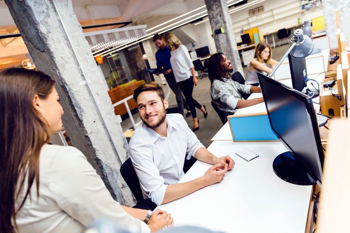 a group of people are sitting at desks in an office talking to each other .