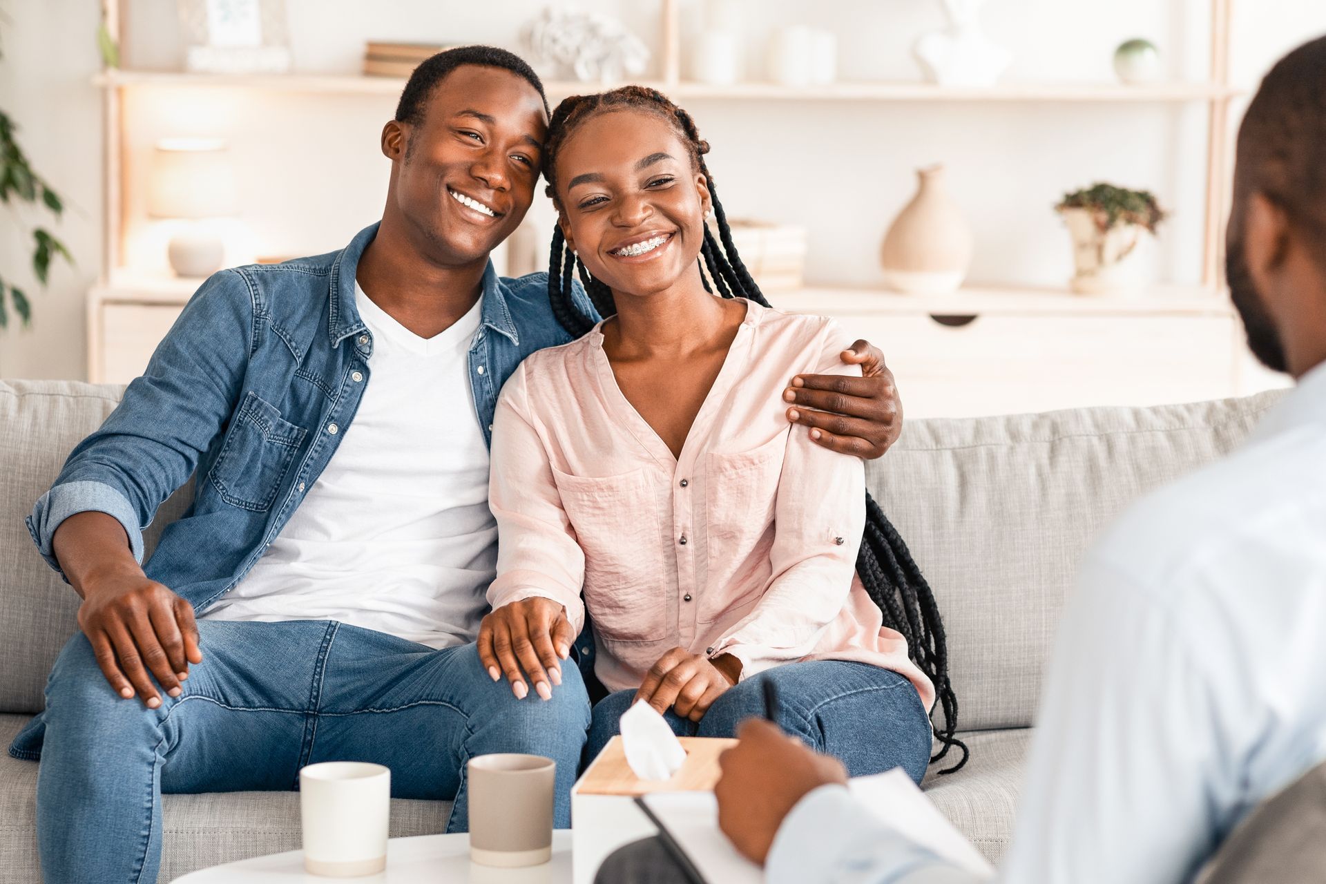 Smiling couple seated on a sofa in a bright living room, talking with a counselor across a coffee table.