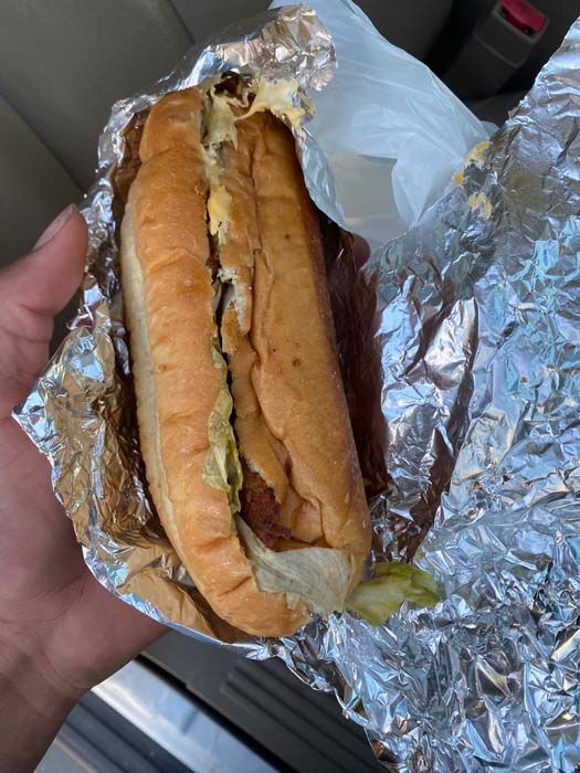 A person is holding a hot dog wrapped in tin foil.