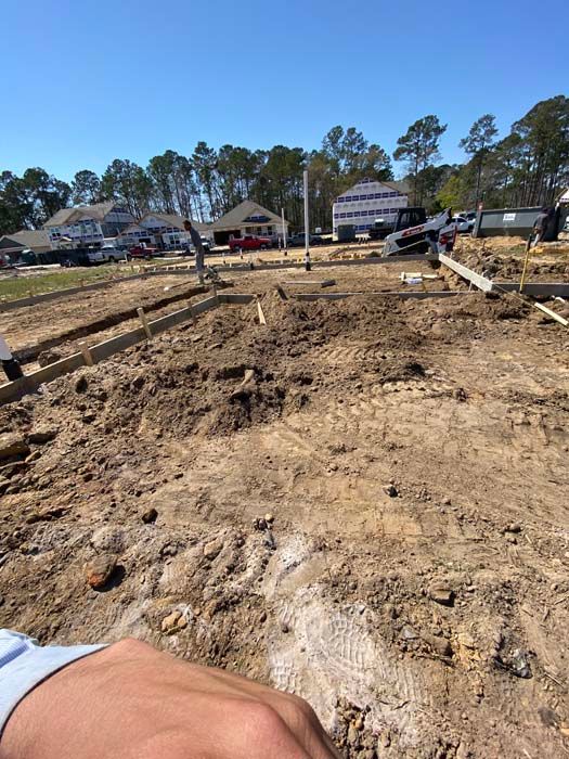 A person is standing in a dirt field with a house in the background.