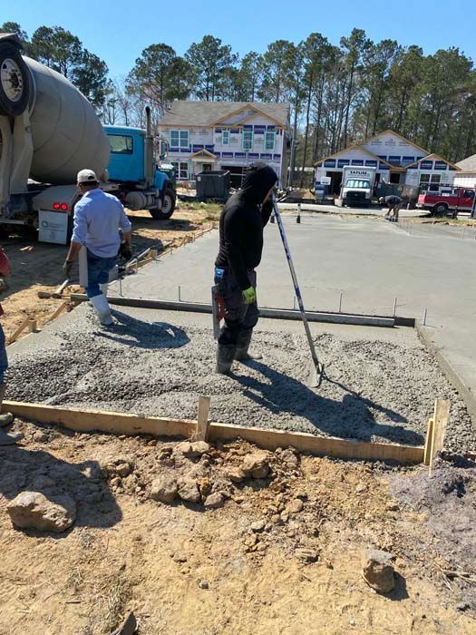 A man is pouring concrete on a sidewalk in front of a cement truck.