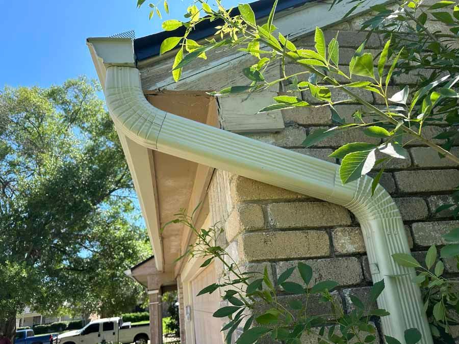A white gutter is attached to the side of a brick house.