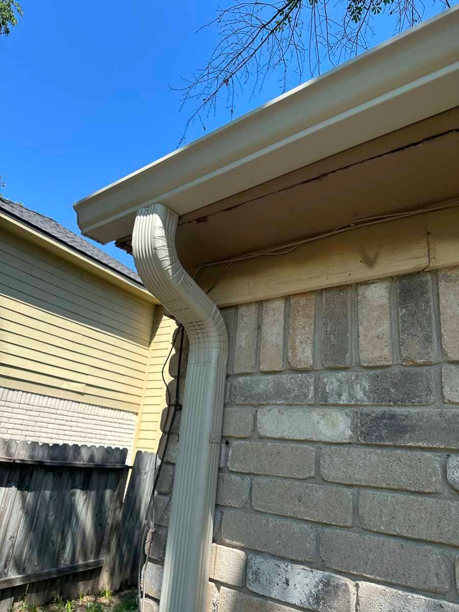 A white gutter on the side of a brick house.