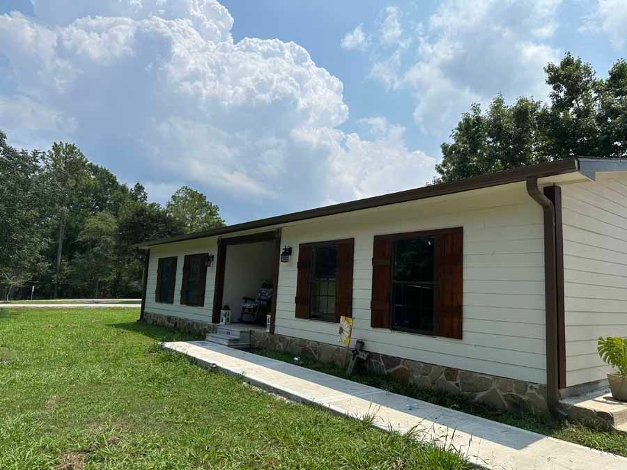 A white house with brown shutters is sitting on top of a lush green field.