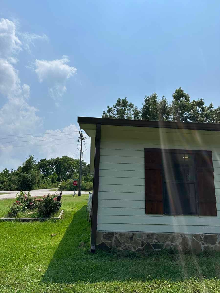 A small white house with brown shutters is sitting in the middle of a lush green field.