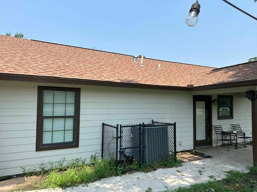 A white house with a brown roof and a fence in front of it.